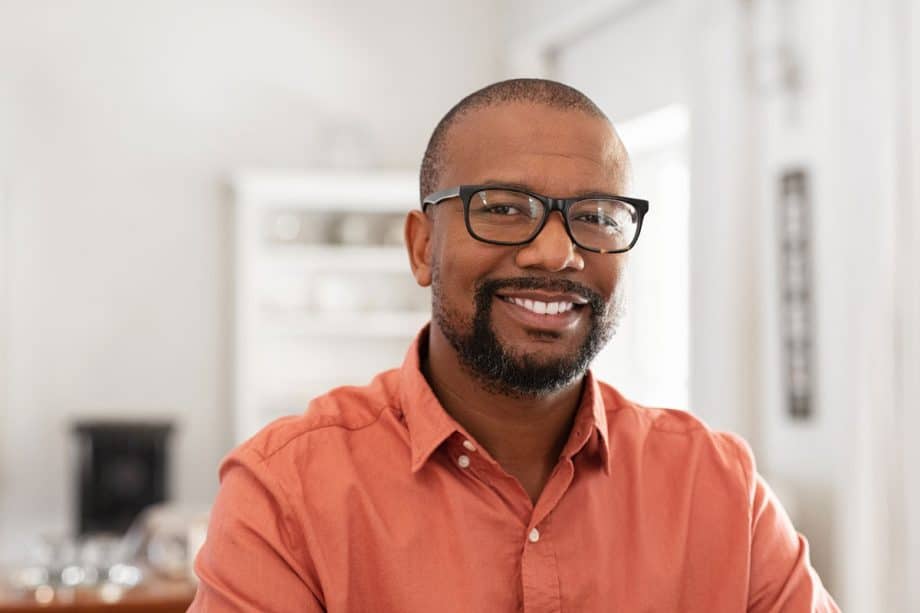 man in orange button down shirt wearing glasses, sitting in living room, smiling